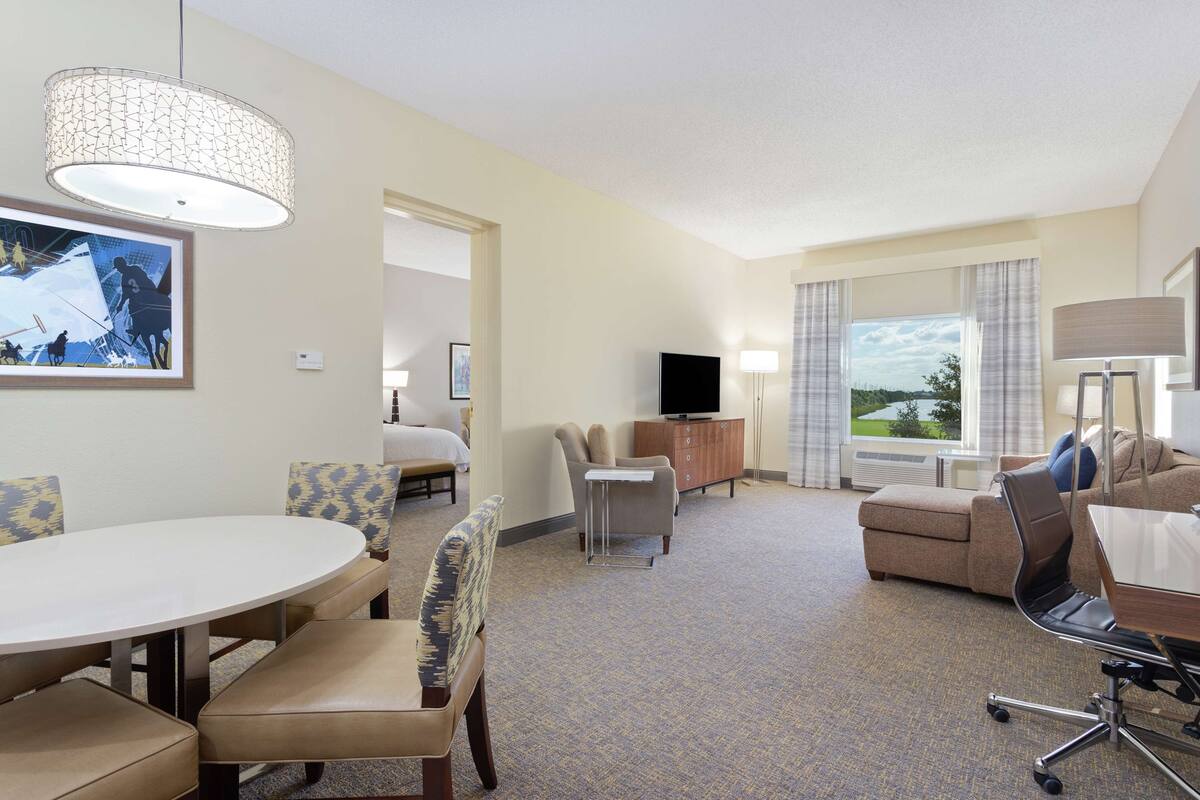 A hotel room with a dining area, a sofa, a TV, and a window with a view.