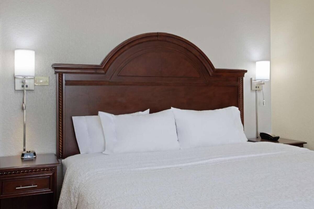 A hotel room with a wooden headboard, white bedding, a bedside table with a lamp, and a phone on the nightstand.