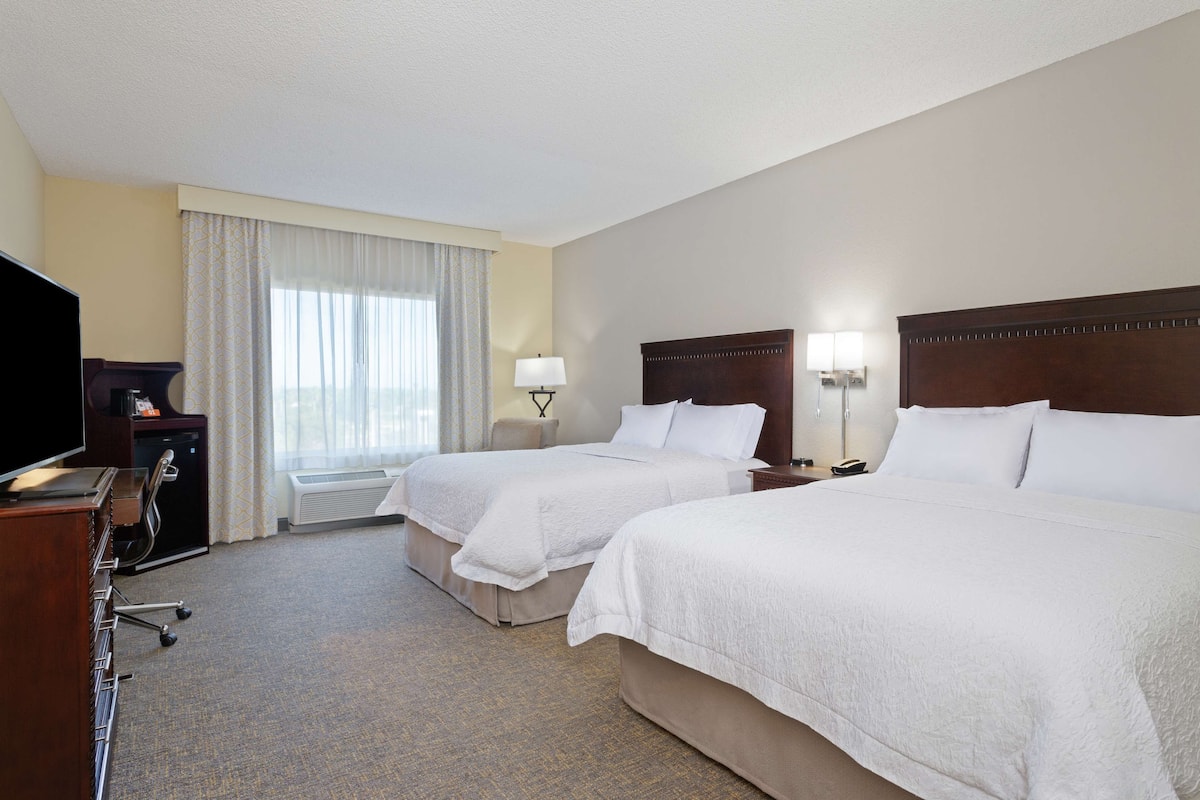 A hotel room with two beds, a TV, a desk, and a lamp.