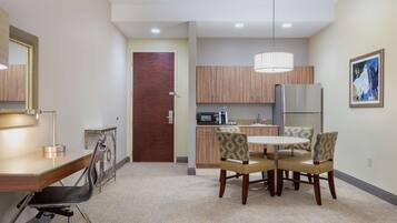 A modern kitchen with wooden cabinets, a refrigerator, and a microwave. There is a dining area with a table and four chairs.