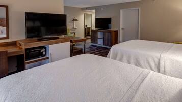 A hotel room with two beds, a TV, a desk with a computer, and a small kitchenette.