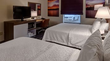 A hotel room with two beds, a desk with a computer, a TV, and artwork on the walls.