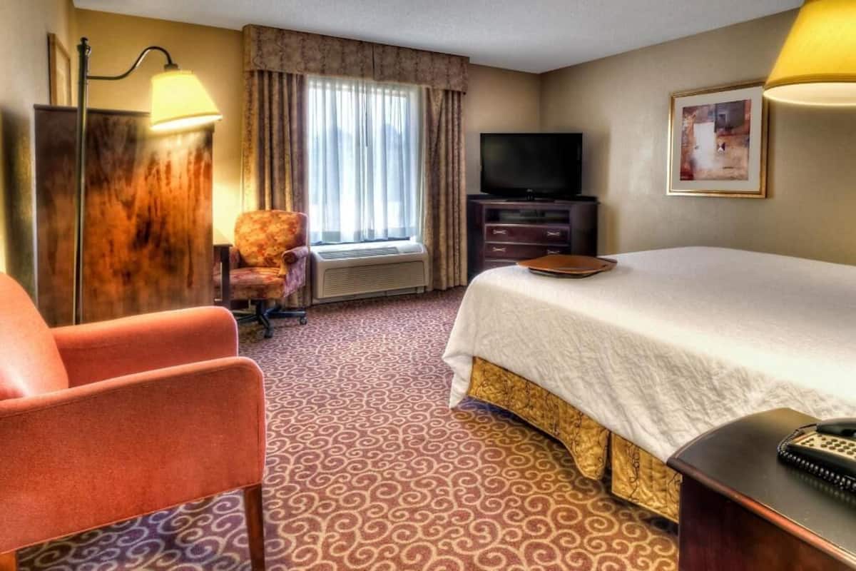 A hotel room with a bed, a television, a desk with a telephone, a chair, and a window with curtains.