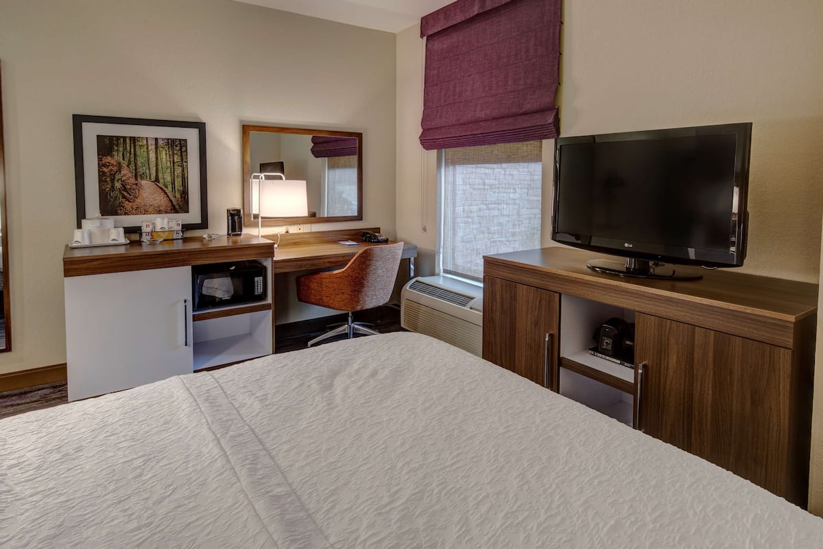 A hotel room with a bed, a desk with a chair, a television, a microwave, and a small refrigerator.
