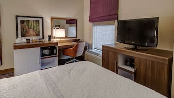 A hotel room with a bed, a desk with a chair, a television, a microwave, and a small refrigerator.