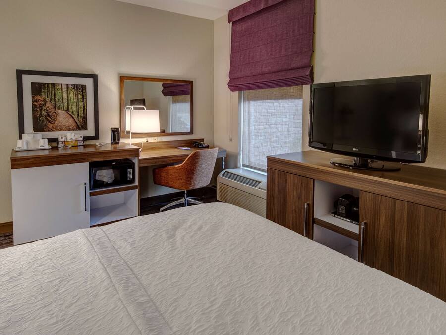 A hotel room with a bed, a desk with a chair, a television, a microwave, and a small refrigerator.