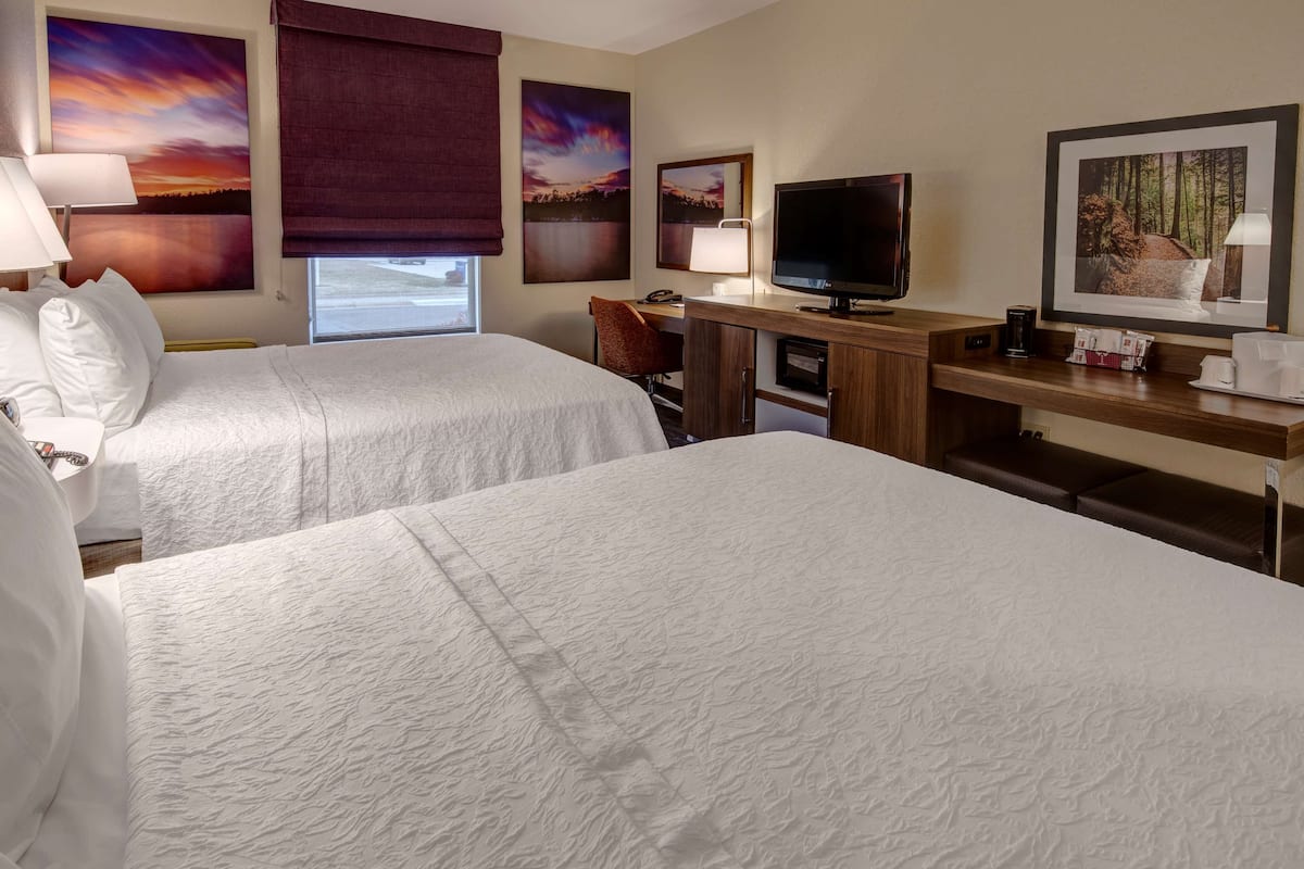 A hotel room with two beds, a desk with a television, and artwork on the walls.
