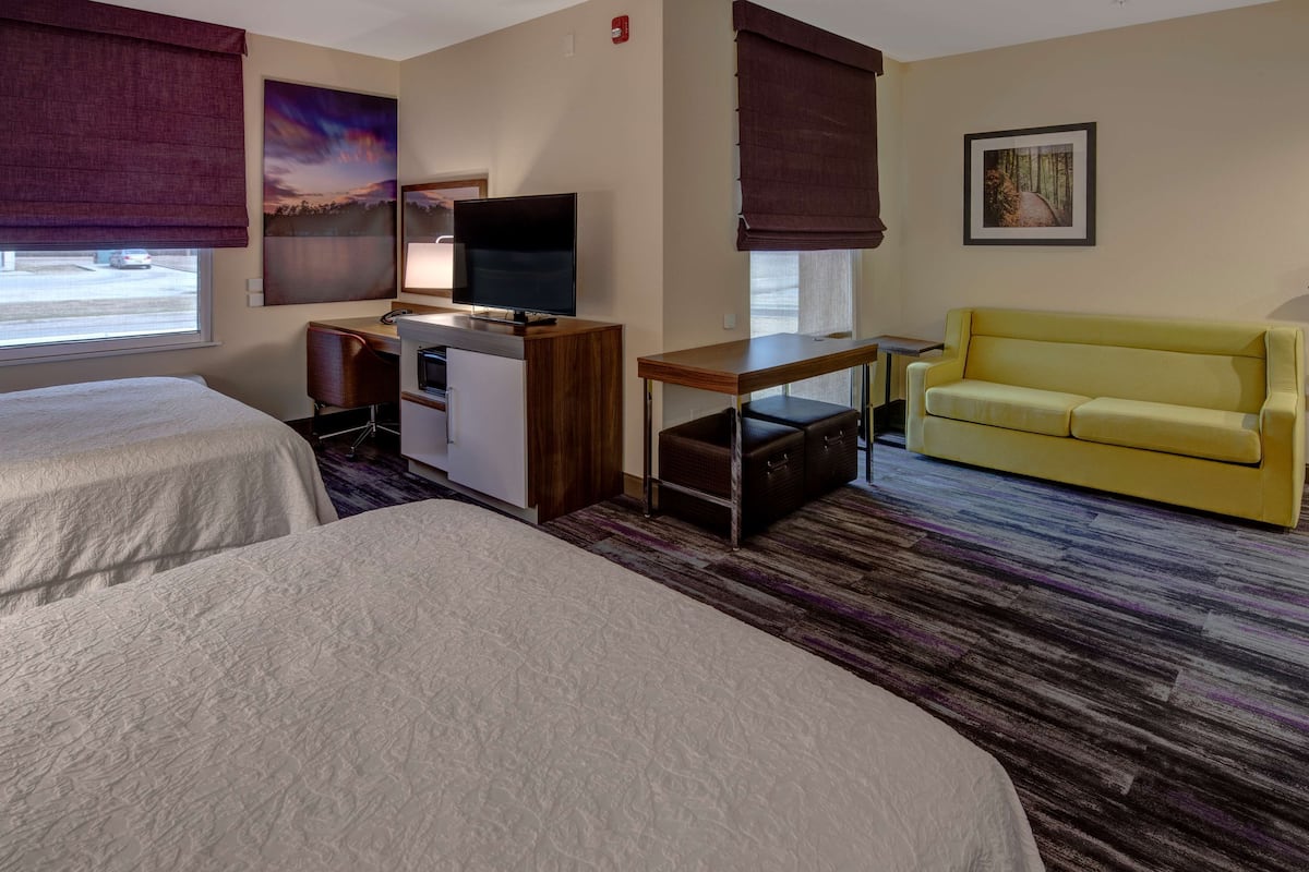 A hotel room with two beds, a desk with a TV, a yellow sofa, and artwork on the walls.