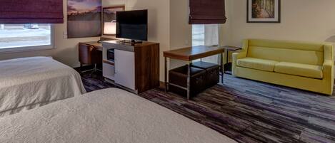 A hotel room with two beds, a desk with a TV, a yellow sofa, and artwork on the walls.