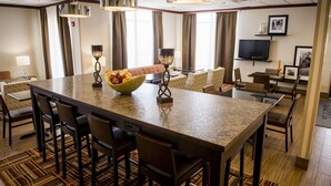 A hotel dining area with a large central island, bar stools, and a television on the wall.