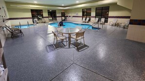 A pool area with lounge chairs and a table, surrounded by walls and a ceiling with lights.
