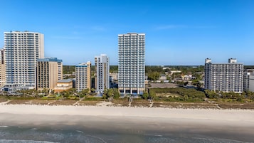 A coastal cityscape with high-rise buildings, a beach, and clear skies.