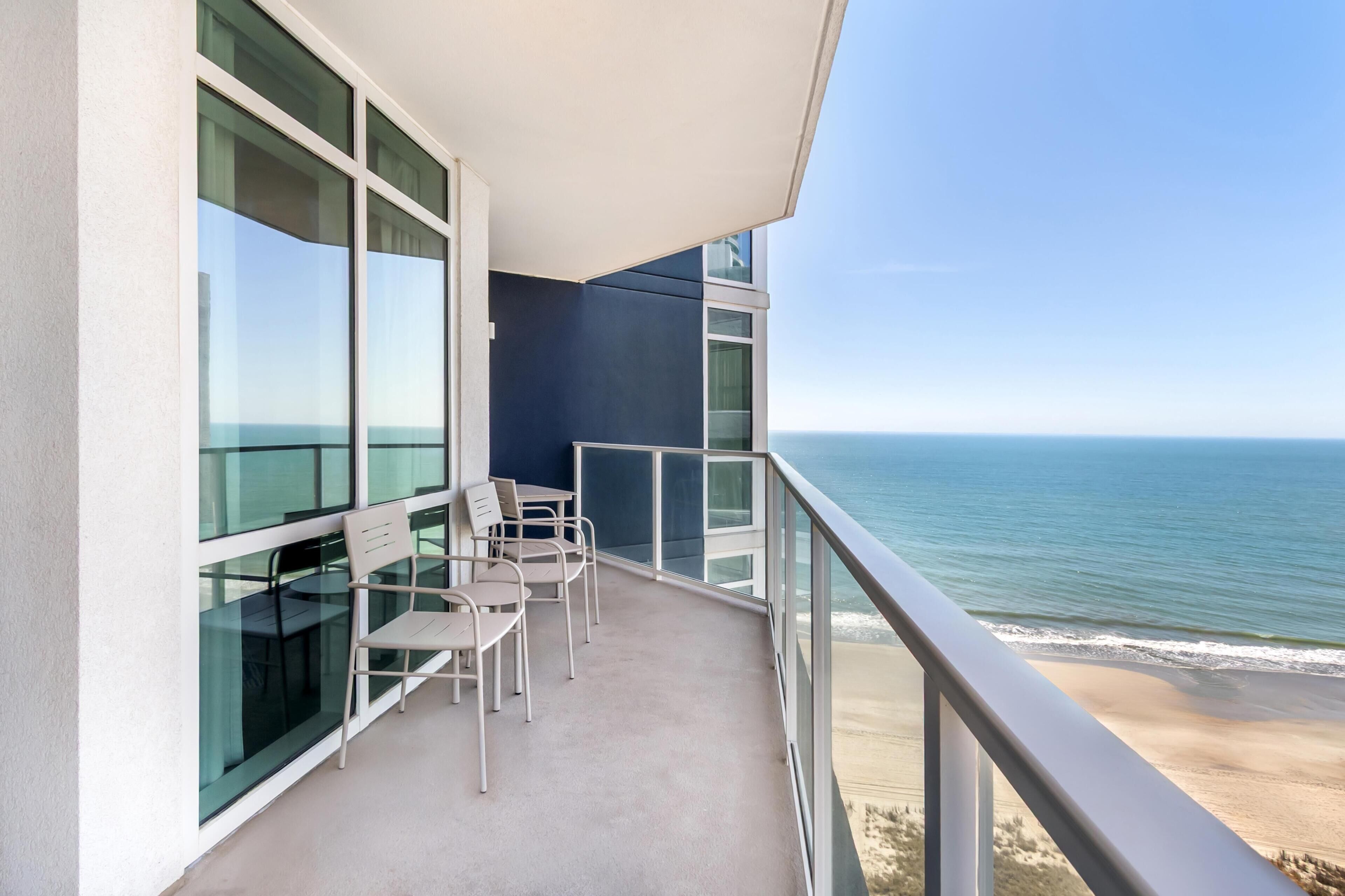 A balcony with a view of the ocean, a table with chairs, and a glass partition.