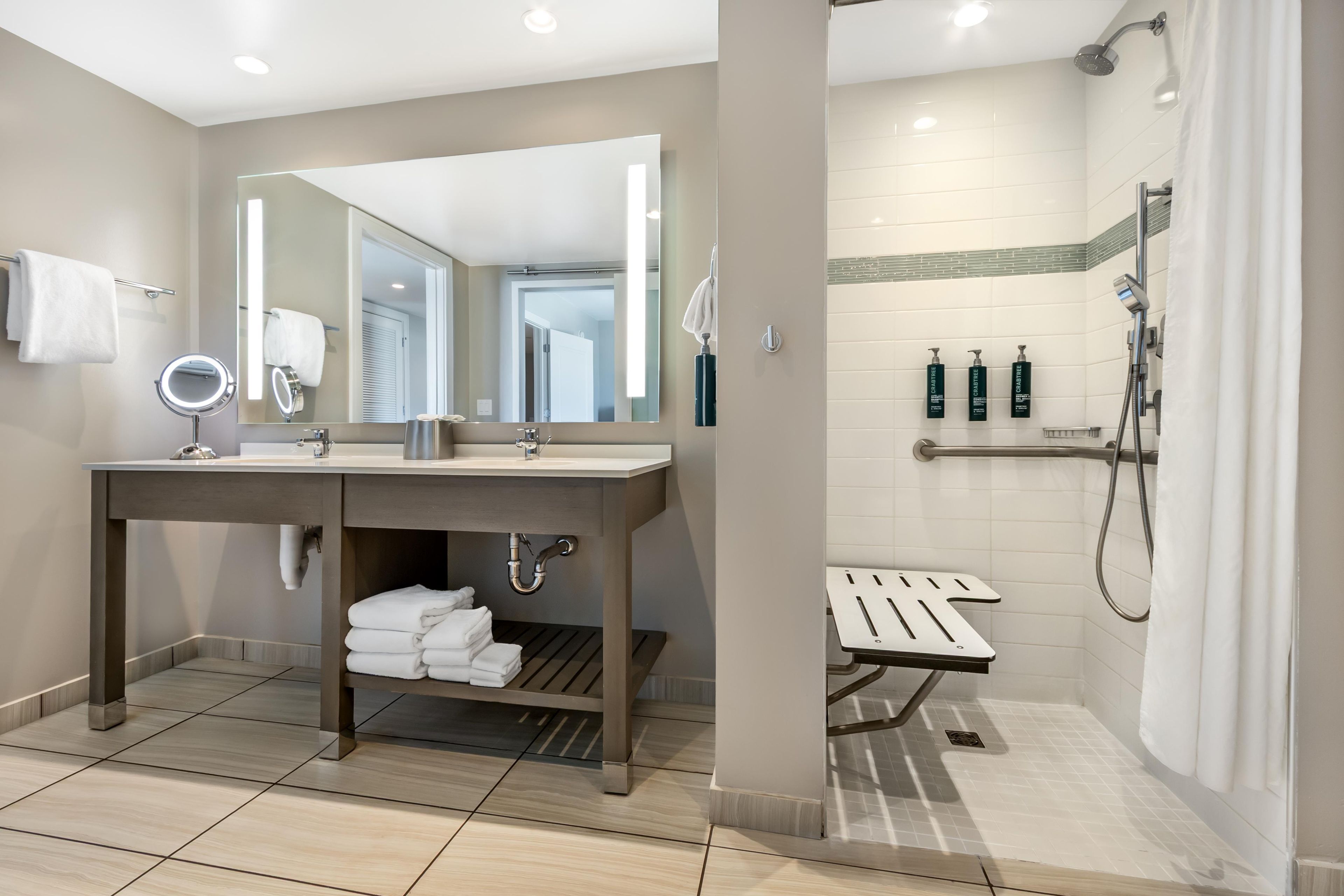 A modern bathroom with a vanity, mirror, towel rack, and shower area.