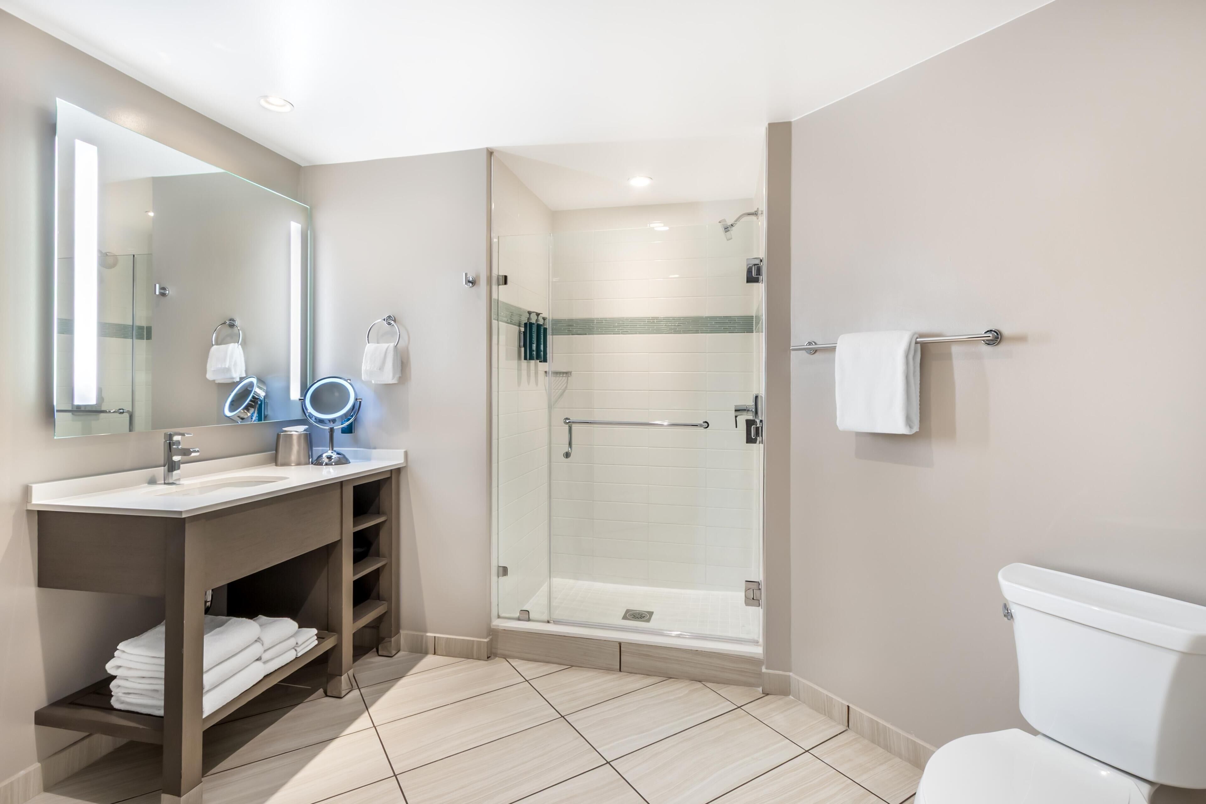 Un baño moderno con ducha de vidrio, tocador con espejo y inodoro.