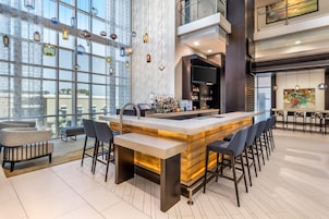A modern bar area with a central island, bar stools, a large window, and a high ceiling.