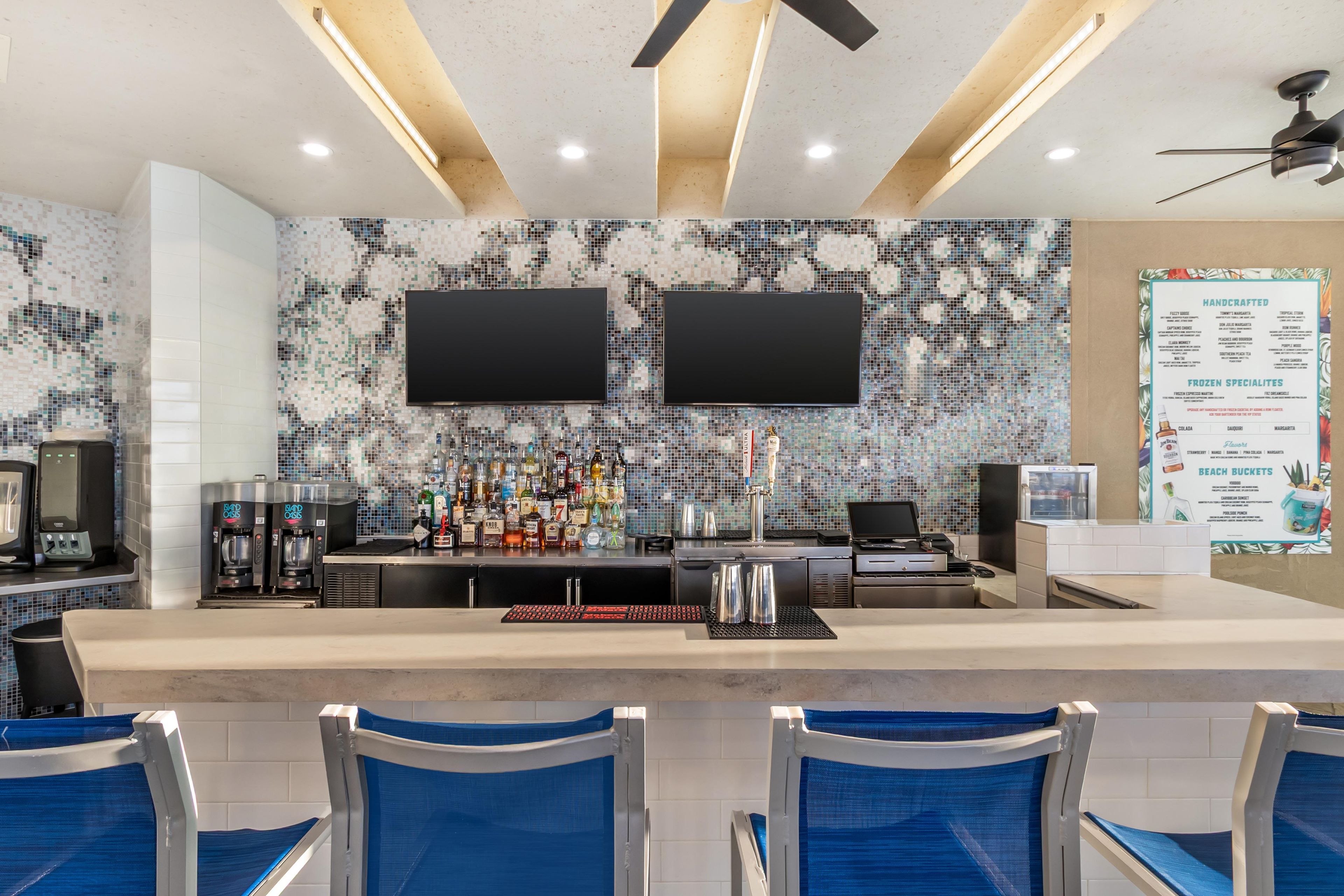 A bar area with a counter, two TVs, a menu board, and blue chairs.