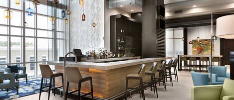 A modern bar area with a central island, bar stools, and a view through large windows.