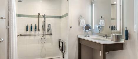 Un baño moderno con ducha, tocador con espejo y artículos de aseo.