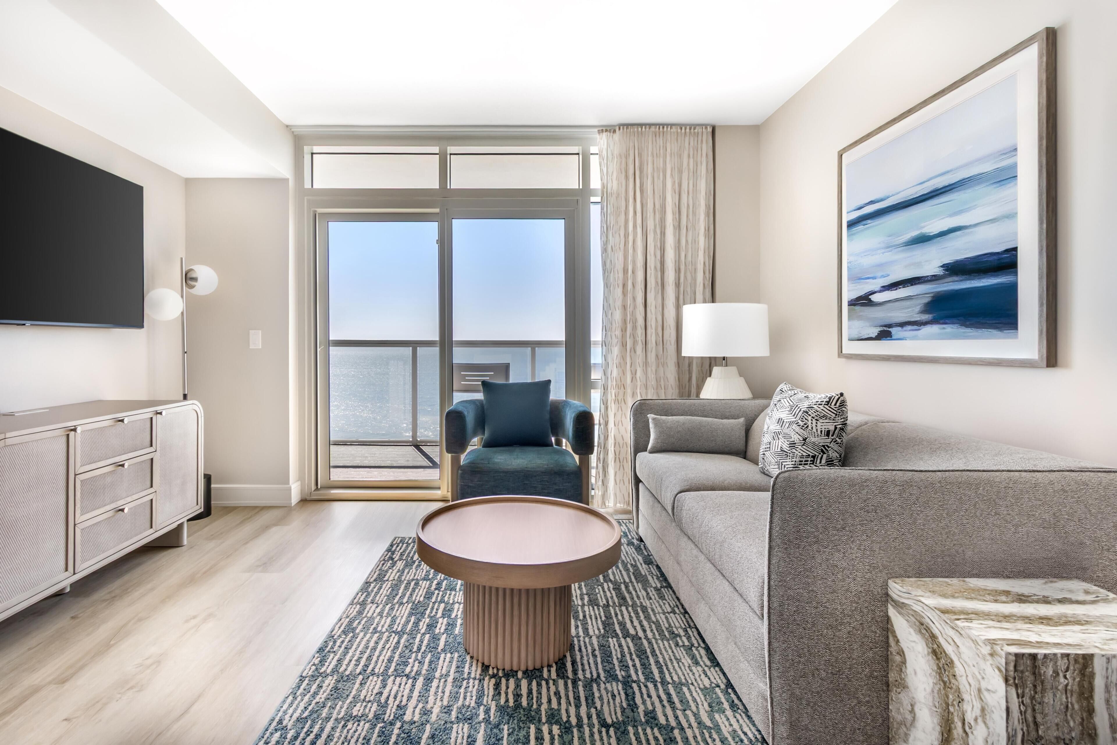 A modern living room with a flat-screen TV, a round coffee table, a sofa, a chair, and a large window with a view.