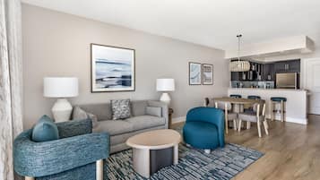 A modern living room with a sofa, armchair, coffee table, and a dining area with a table and chairs.