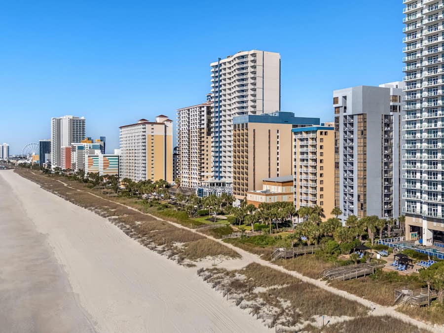 Ein Küstenhotel mit mehreren Hochhäusern, einem Sandstrand und wolkenlosem, blauem Himmel.