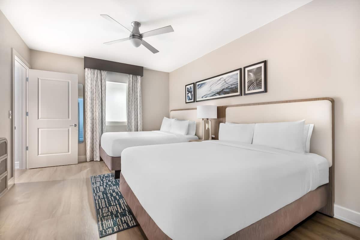 Ett hotellrum med två sängar, en takfläkt, en dörr och ett fönster med gardiner.
