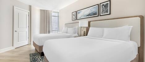 A hotel room with two beds, a ceiling fan, a window with curtains, and framed artwork on the wall.