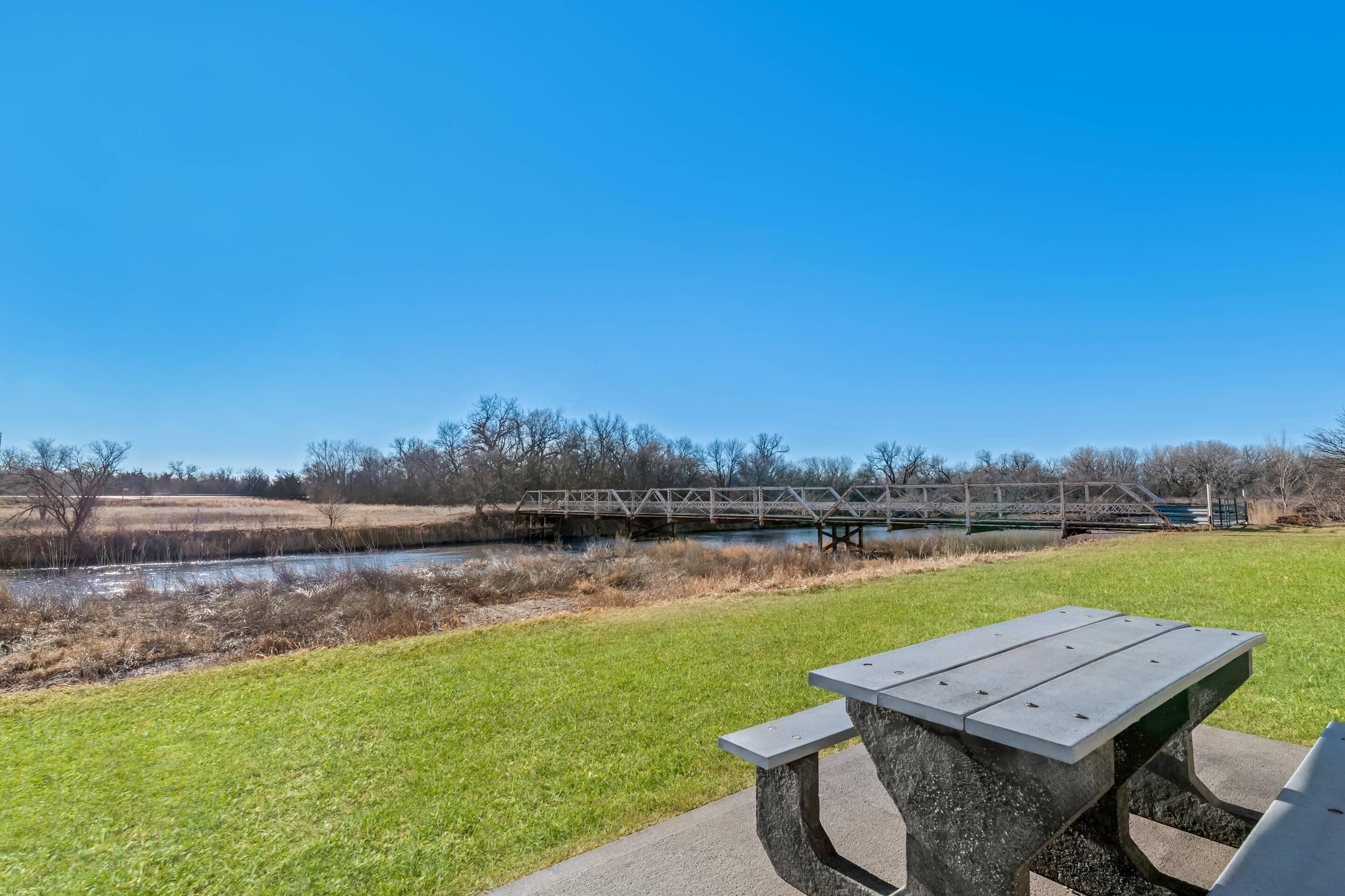 Una mesa de picnic en un parque, con un río y un puente al fondo.