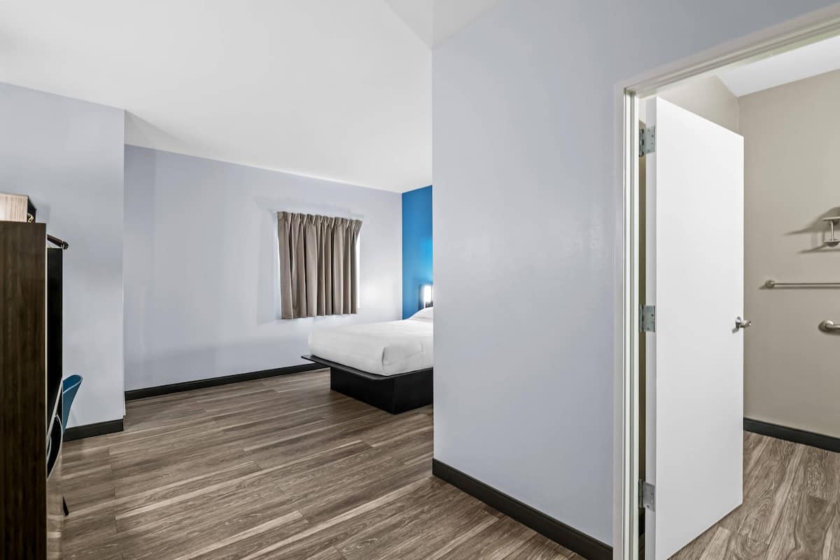 A hotel room with a bed, a wardrobe, and a door leading to another room.