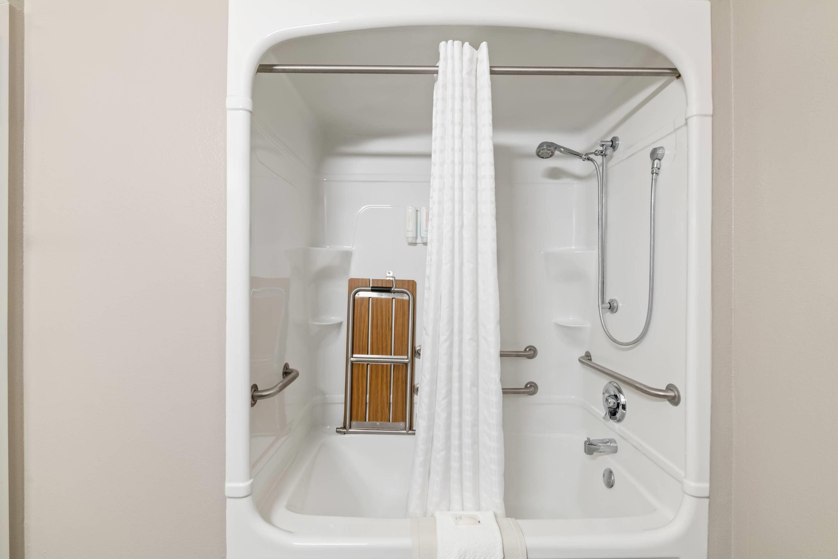 A bathroom with a bathtub, shower, and grab bars.