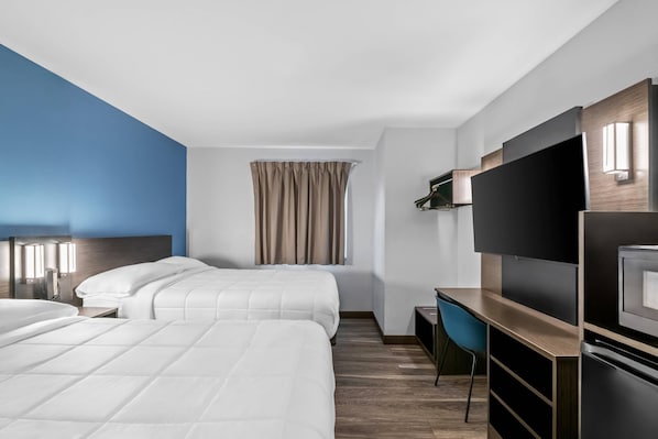 A hotel room with two beds, a desk, a TV, and a window with curtains.