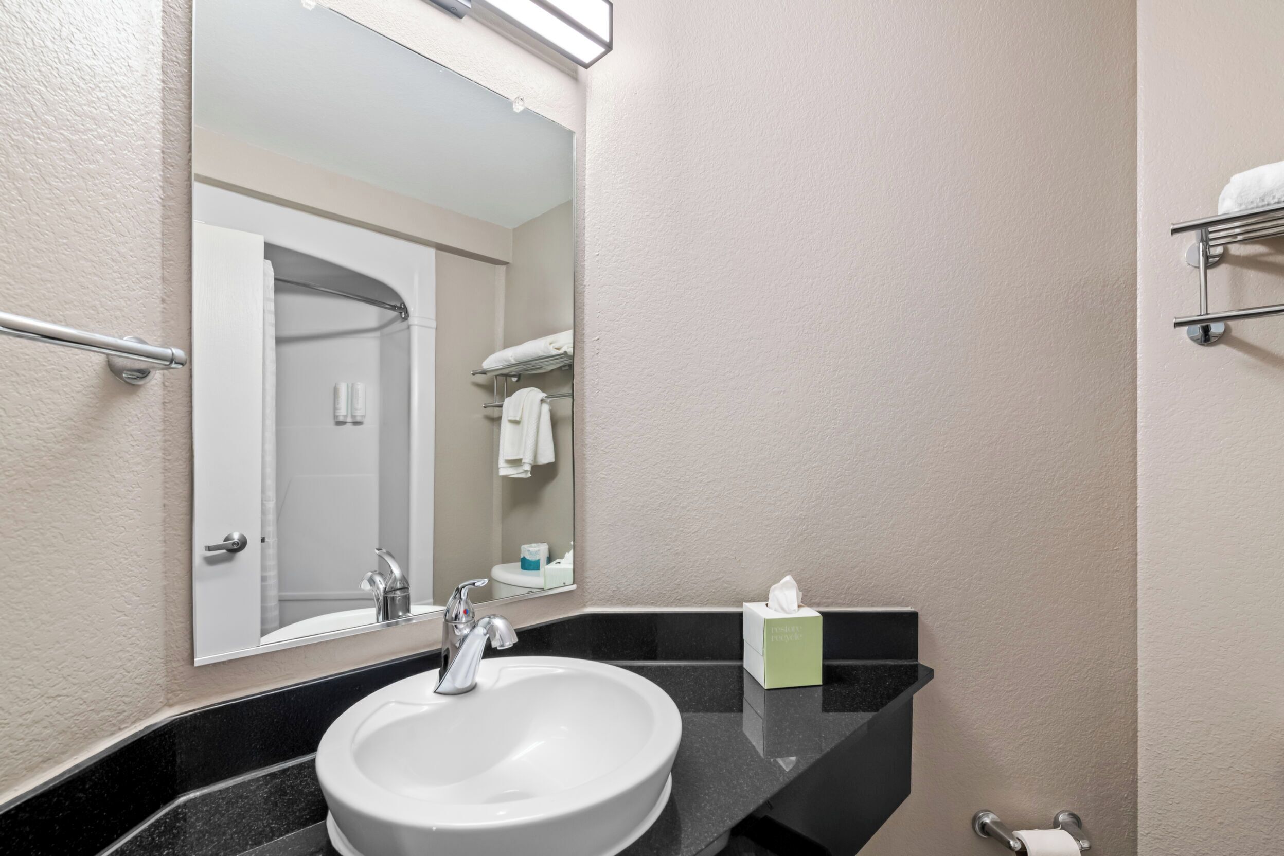 A bathroom with a white sink, a mirror, a towel rack, and a tissue box.