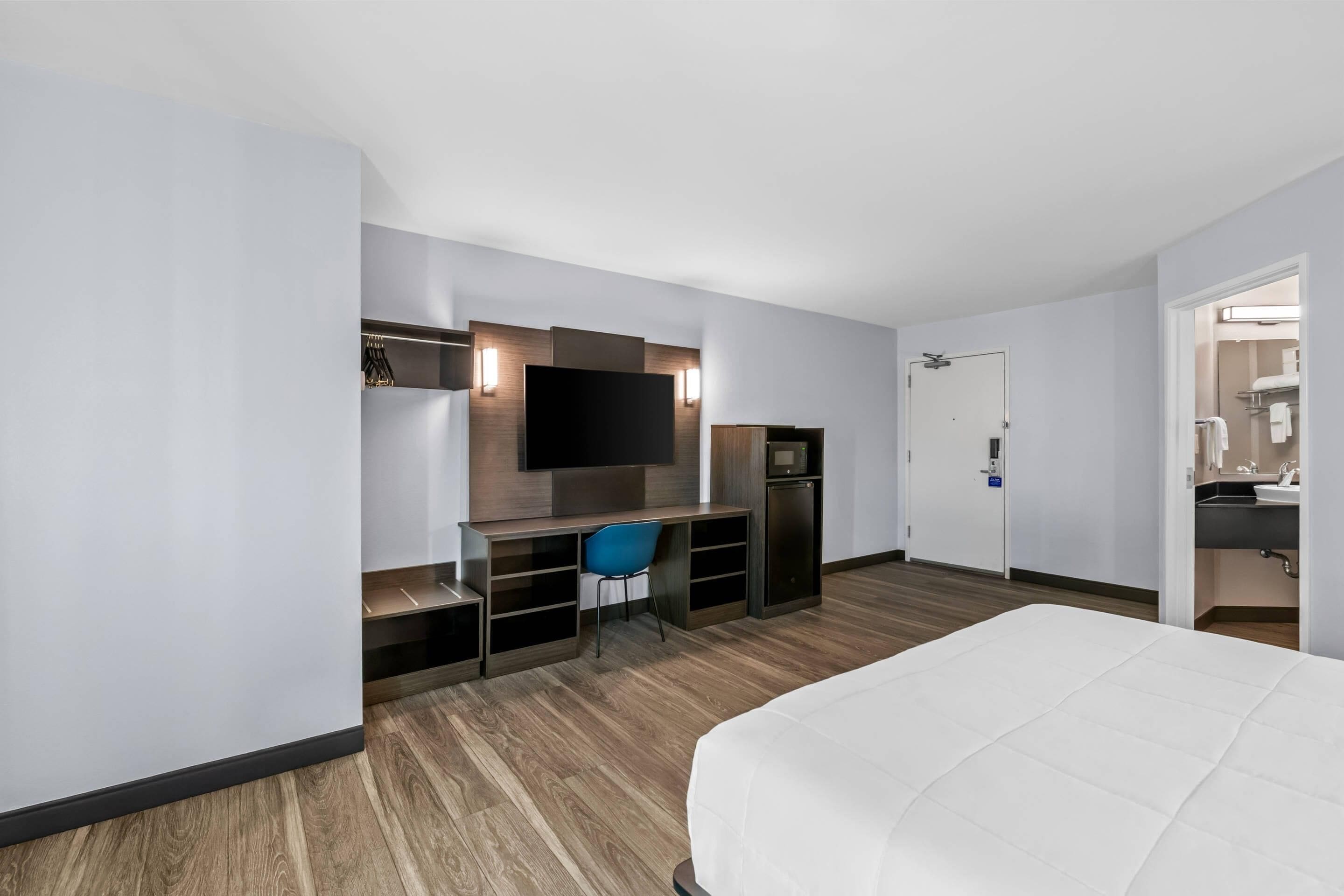 Une chambre d’hôtel comprenant un lit, un bureau avec une chaise, une télévision et une petite kitchenette.