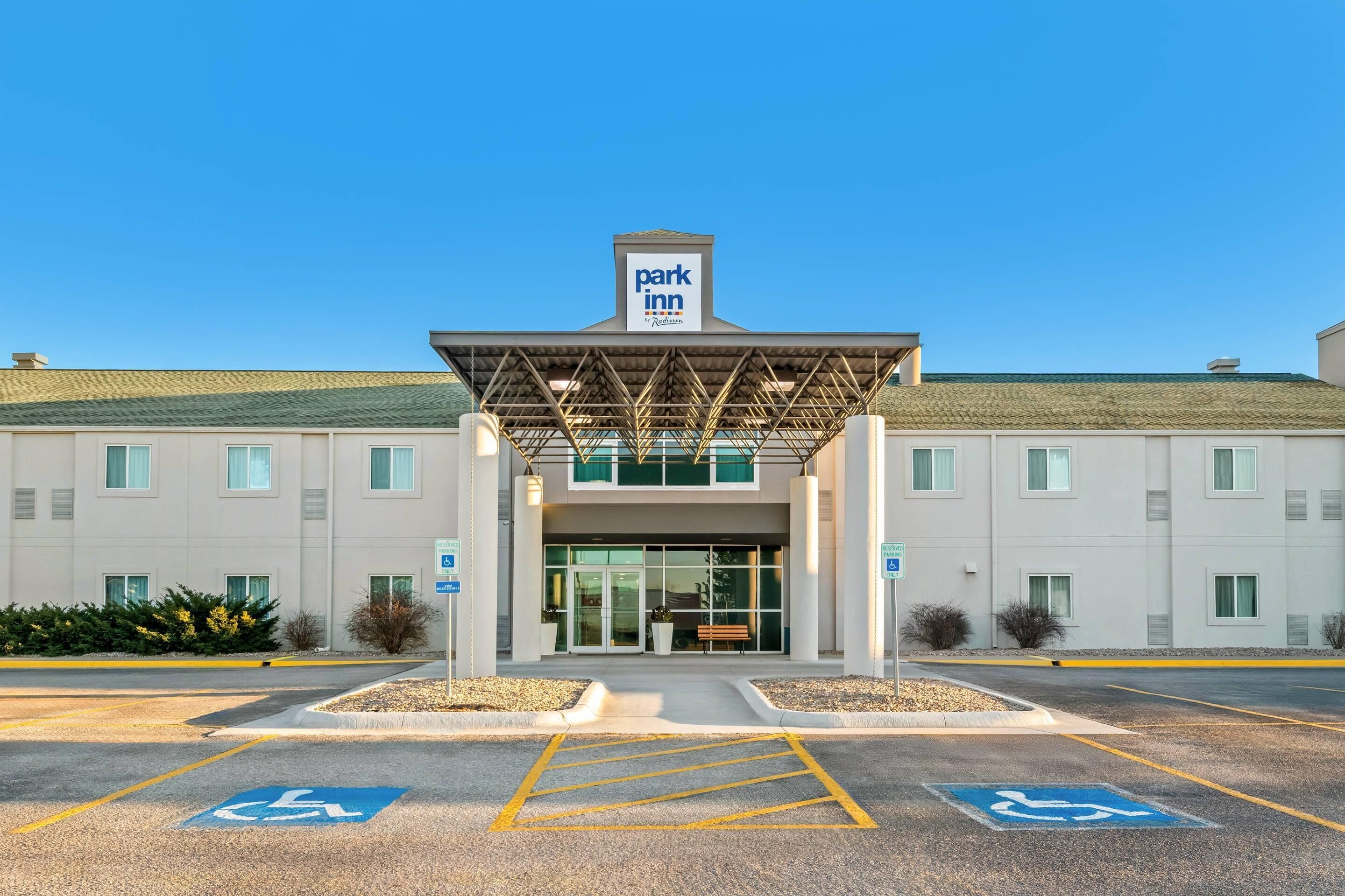 A Park Inn hotel entrance with a covered walkway, handicap parking, and a clear blue sky.