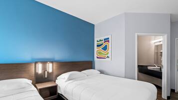 Habitación de hotel con dos camas, una pared de acento azul, una lámpara moderna y un baño visible a través de una puerta abierta.