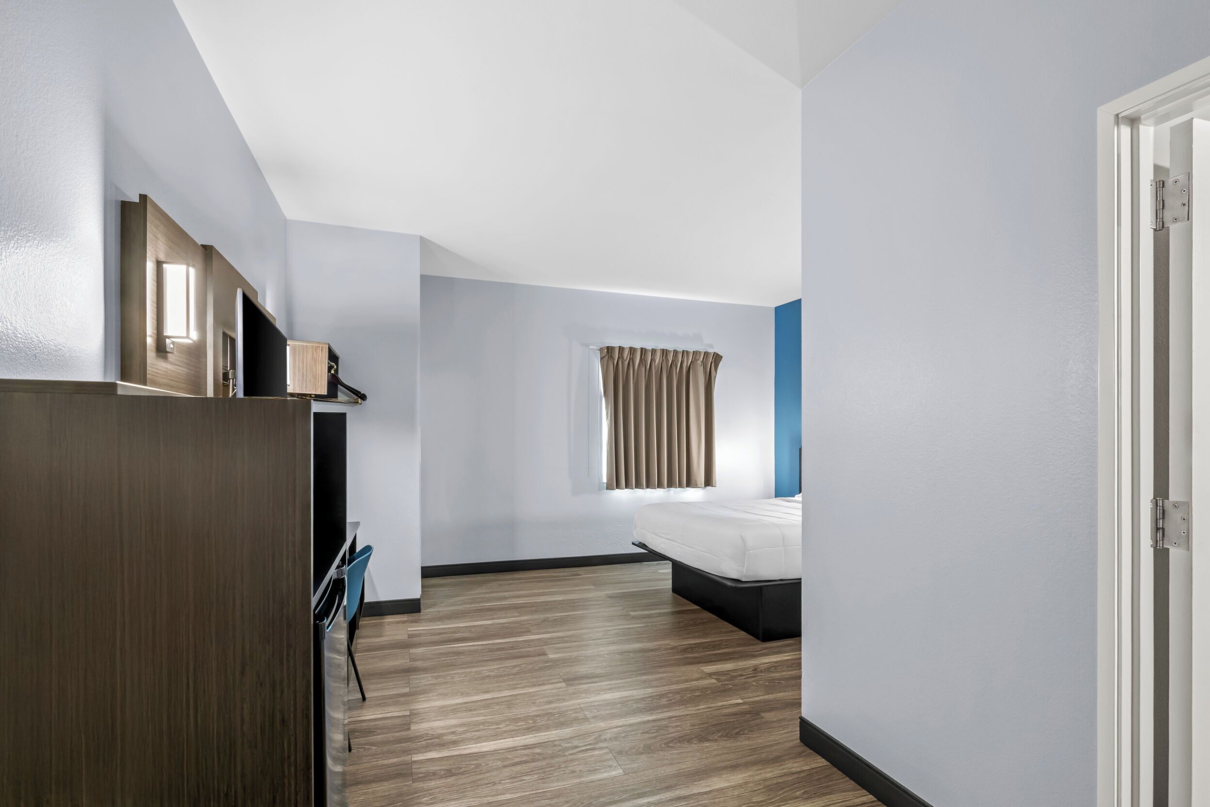 Ein Hotelzimmer mit Bett, Schreibtisch, Stuhl, einem Fenster mit Vorhängen und einer Tür.