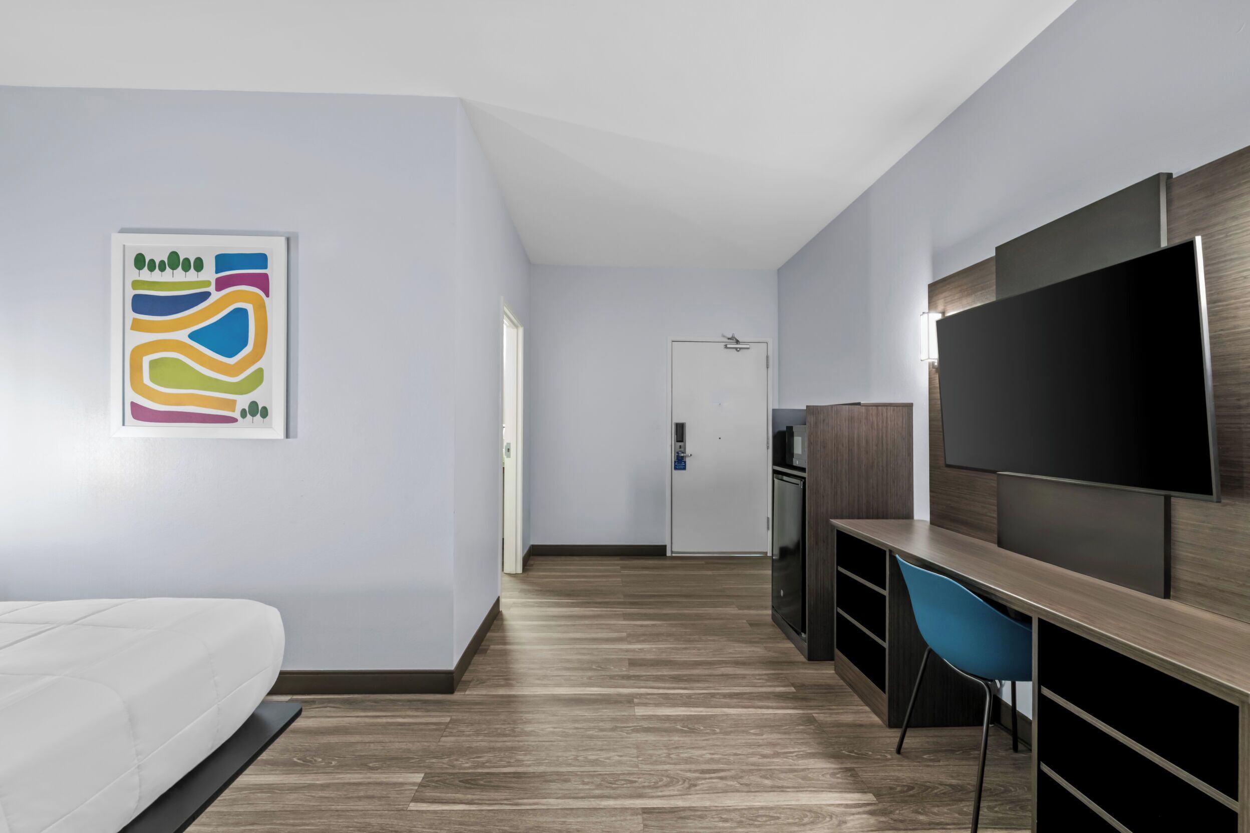 A modern hotel room with a bed, a desk with a chair, a flat-screen TV, and a wall-mounted artwork.