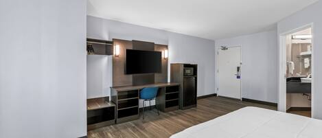 Ein Hotelzimmer mit einem Bett, einem Schreibtisch mit Stuhl, einem Fernseher und einer kleinen Küchenzeile.