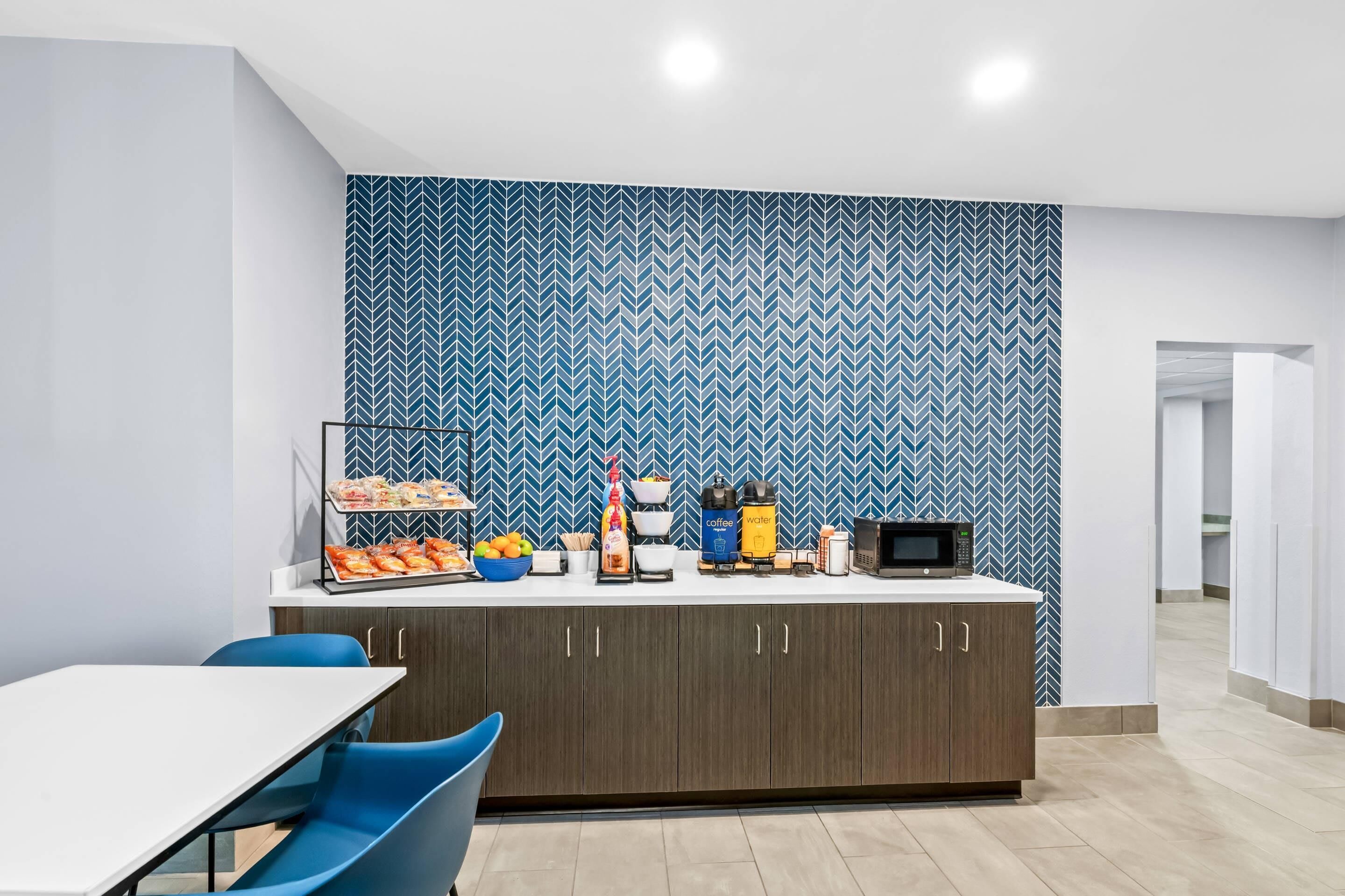 A modern kitchen with a herringbone-patterned backsplash, a coffee station, and a dining area with blue chairs.