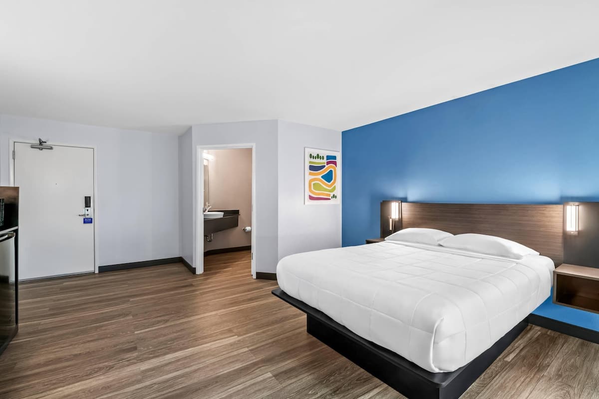 A modern hotel room with a bed, a desk, and a bathroom visible through an open door.