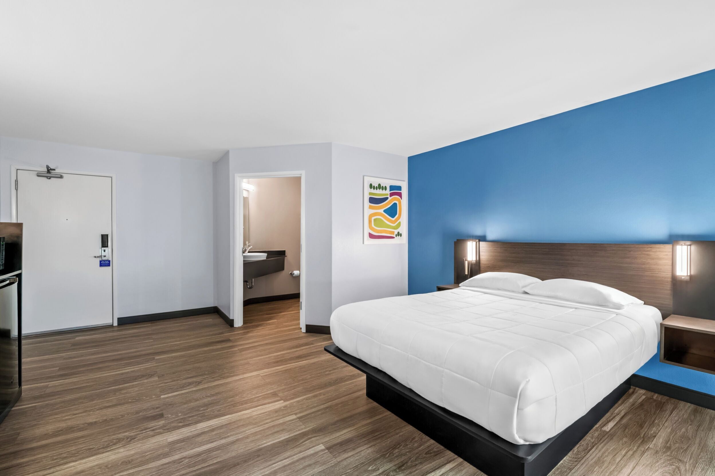 Una habitación de hotel moderna con cama, mesitas de noche, baño y un pasillo.