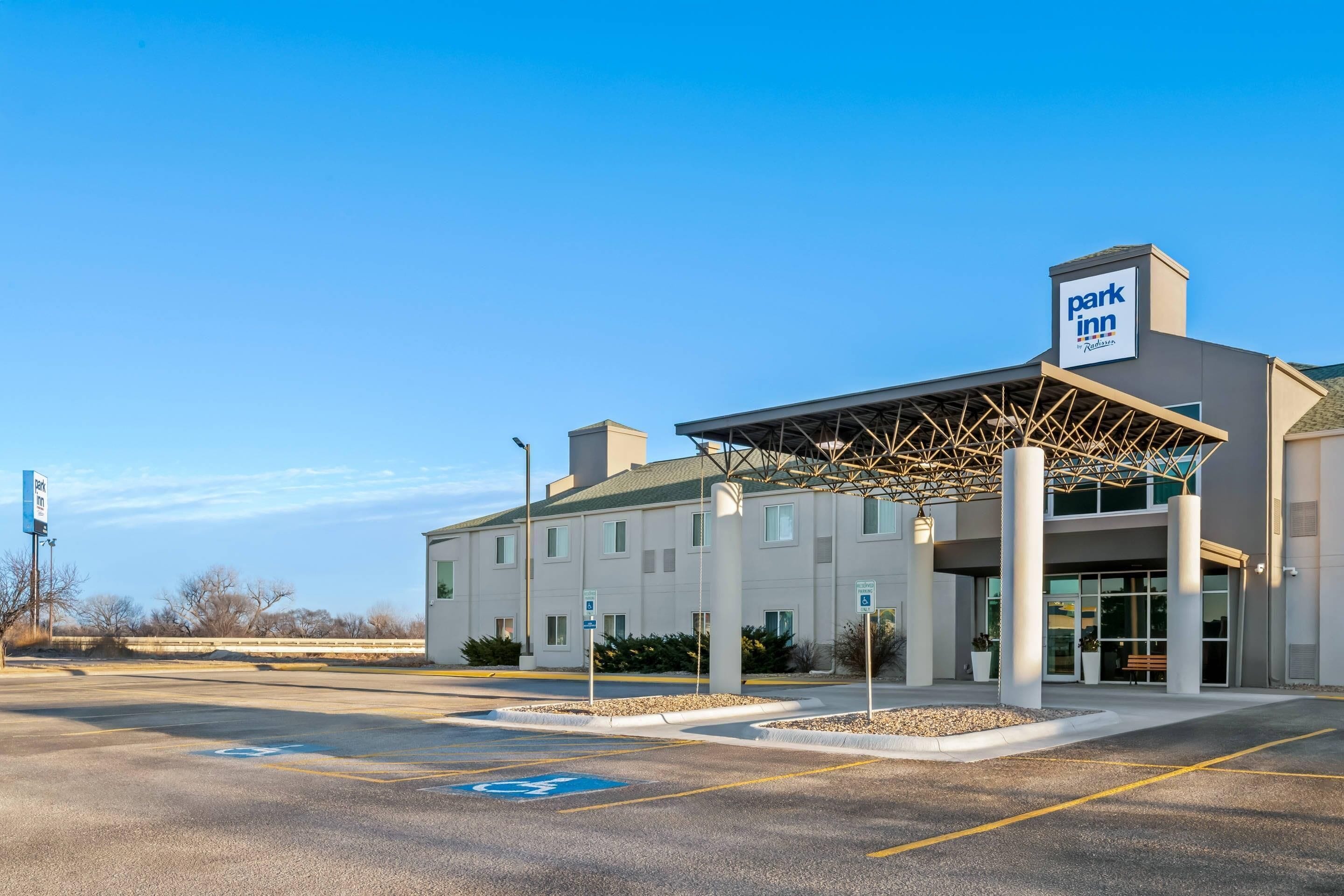 A Park Inn hotel with a covered entrance, a parking lot, and a clear blue sky.