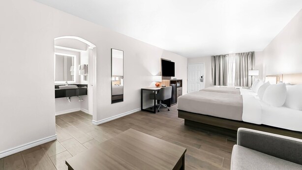 Una habitación de hotel moderna con una cama grande, un escritorio con silla, televisor de pantalla plana y baño con espejo y lavamanos.