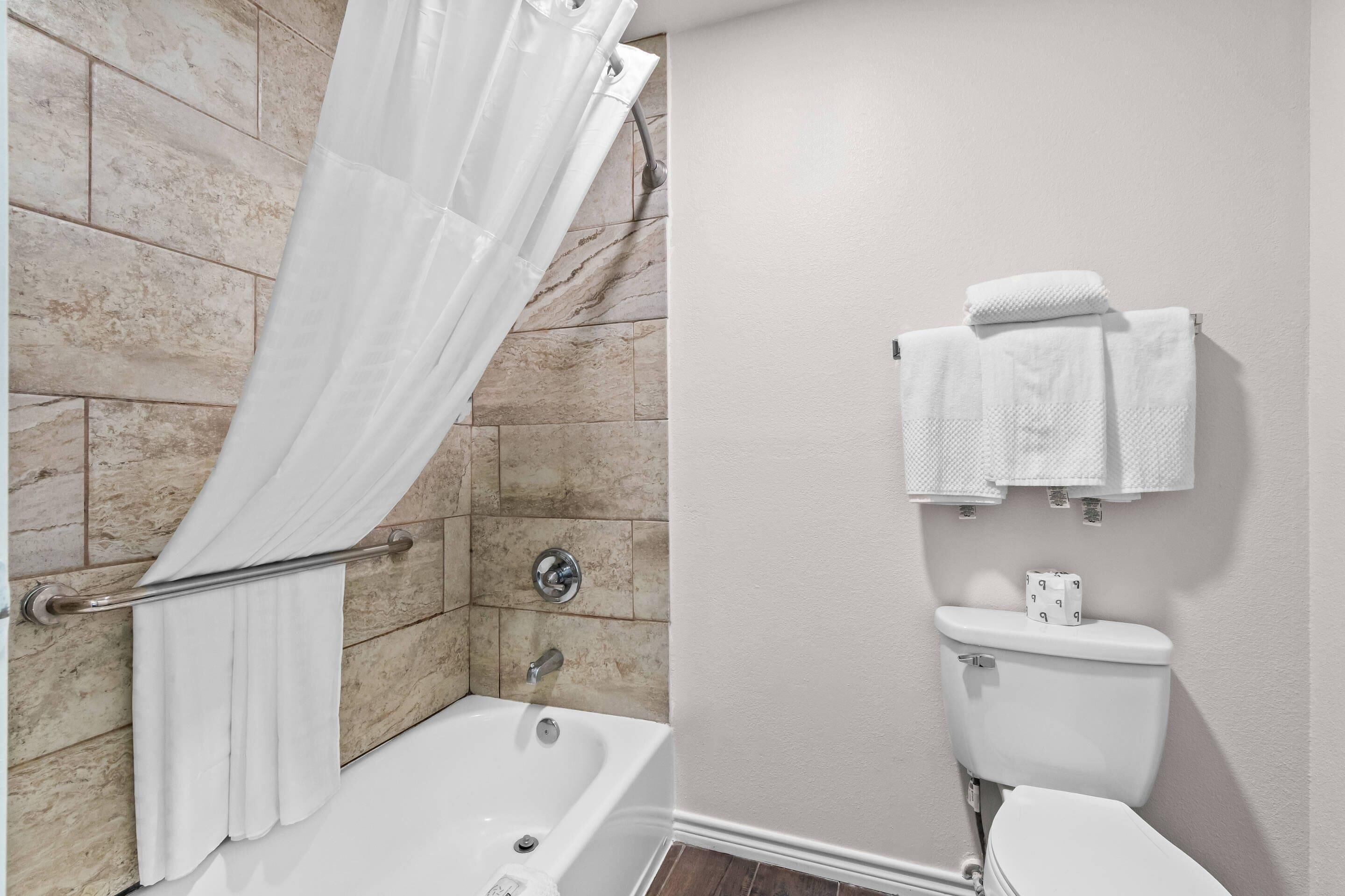 A bathroom with a bathtub, shower curtain, towel rack, toilet, and marble tiles.