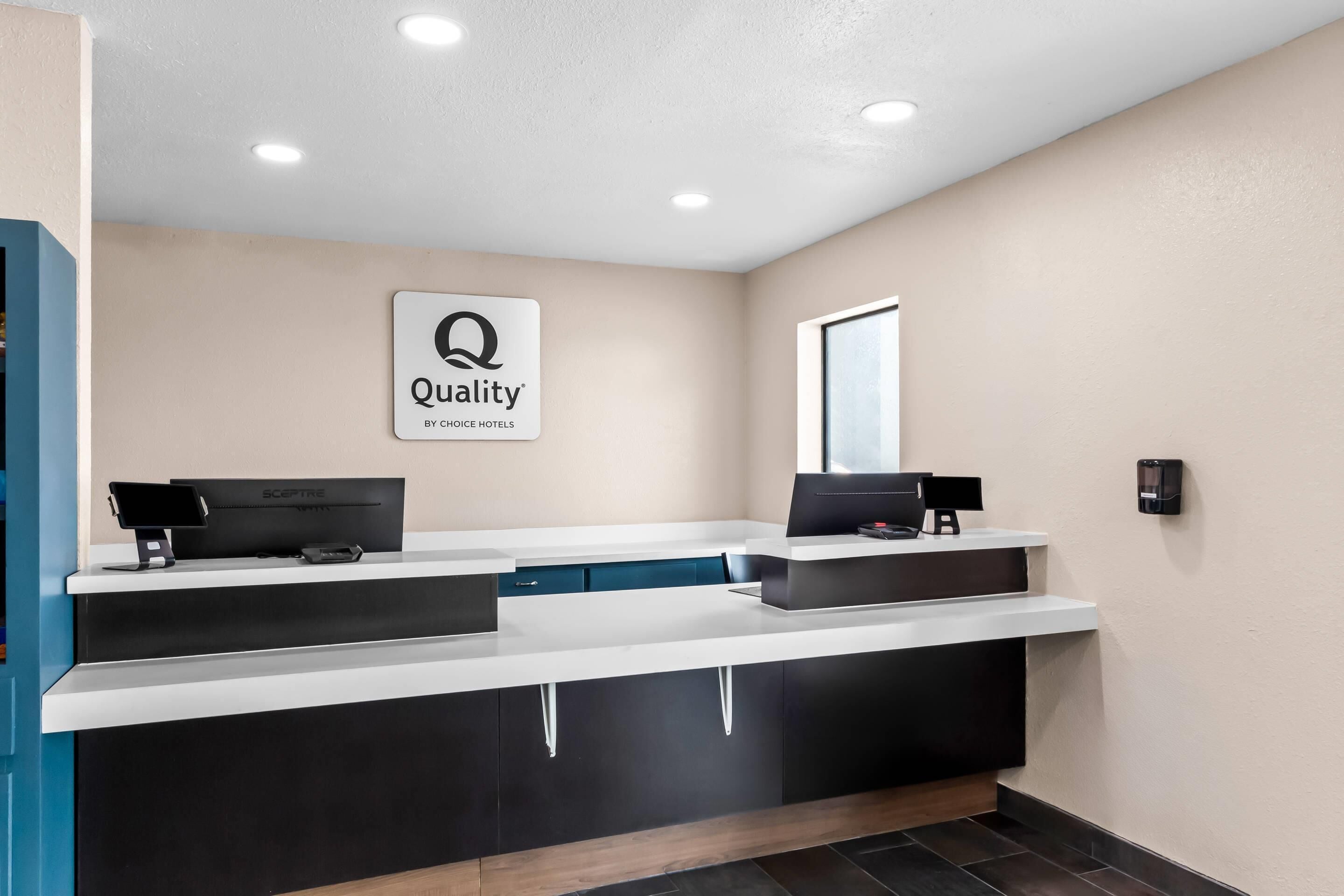 Un espace d’accueil d’hôtel avec une enseigne indiquant « Qualité garantie par Choice Hotels », un comptoir d’accueil, un ordinateur et un appareil fixé au mur.
