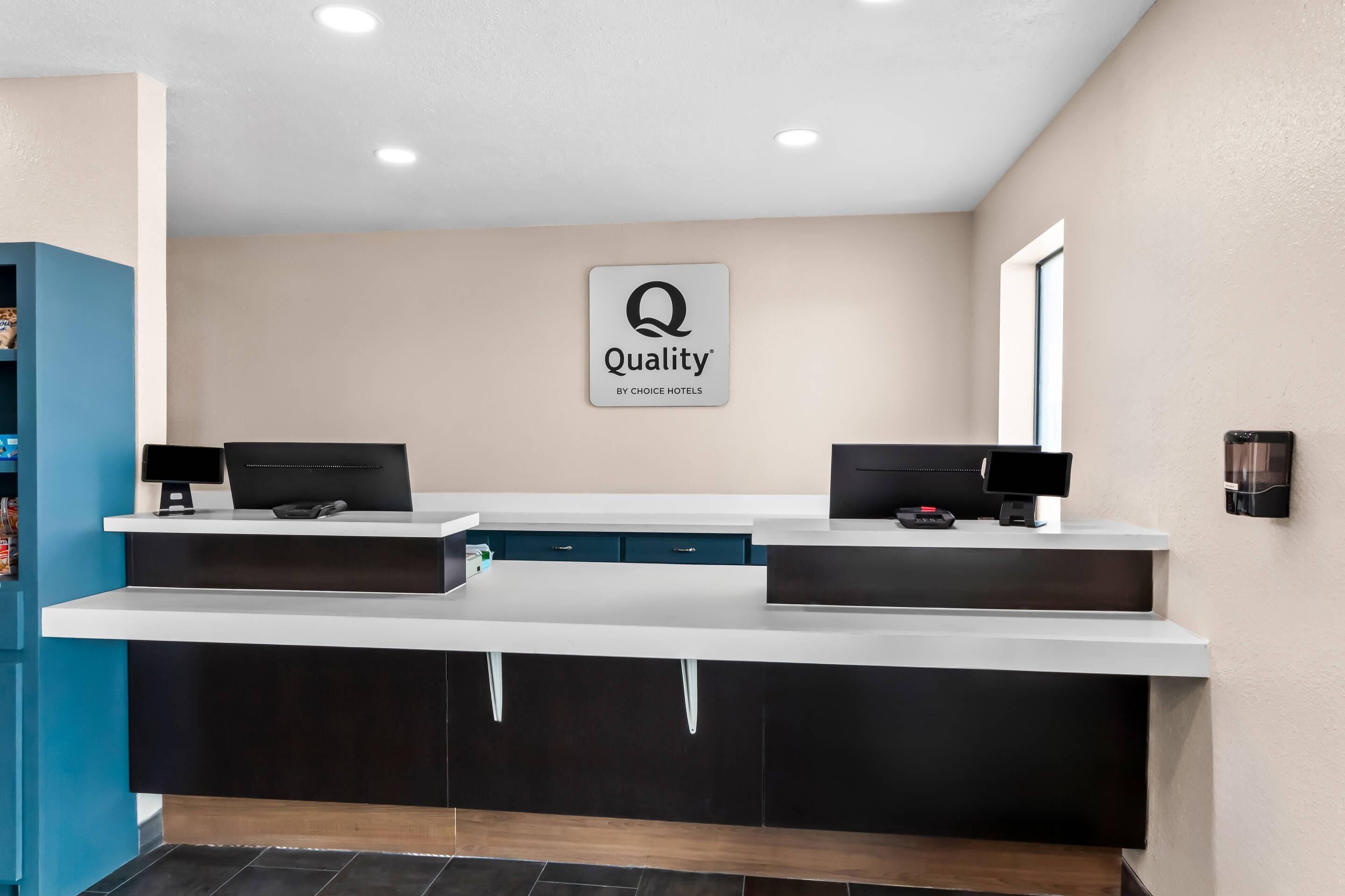 Un comptoir d’accueil d’hôtel avec une enseigne « Quality by Choice Hotels », deux écrans d’ordinateur et un écran numérique.