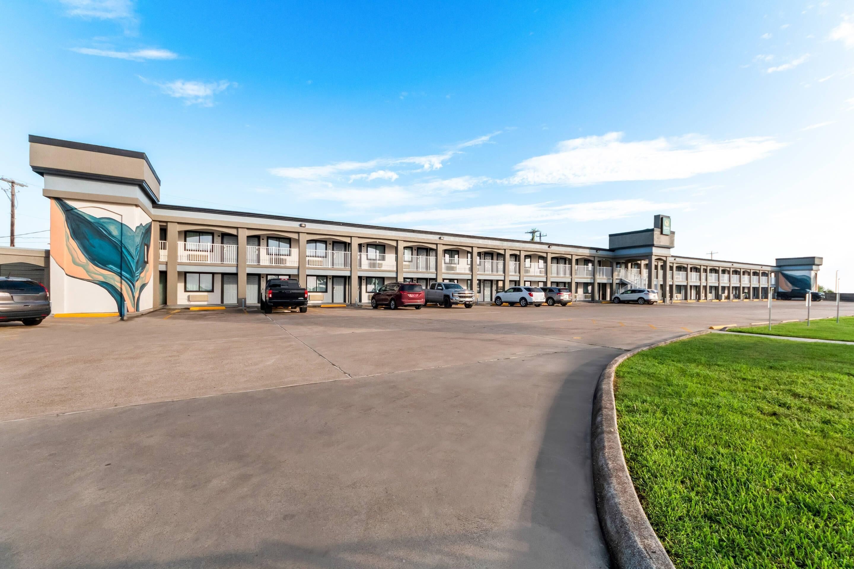 A motel with a row of rooms, a parking lot, and a grassy area.