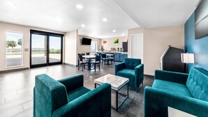 Un moderno vestíbulo de hotel con sofás color turquesa, una mesa de centro de mármol y una zona de cocina al fondo.