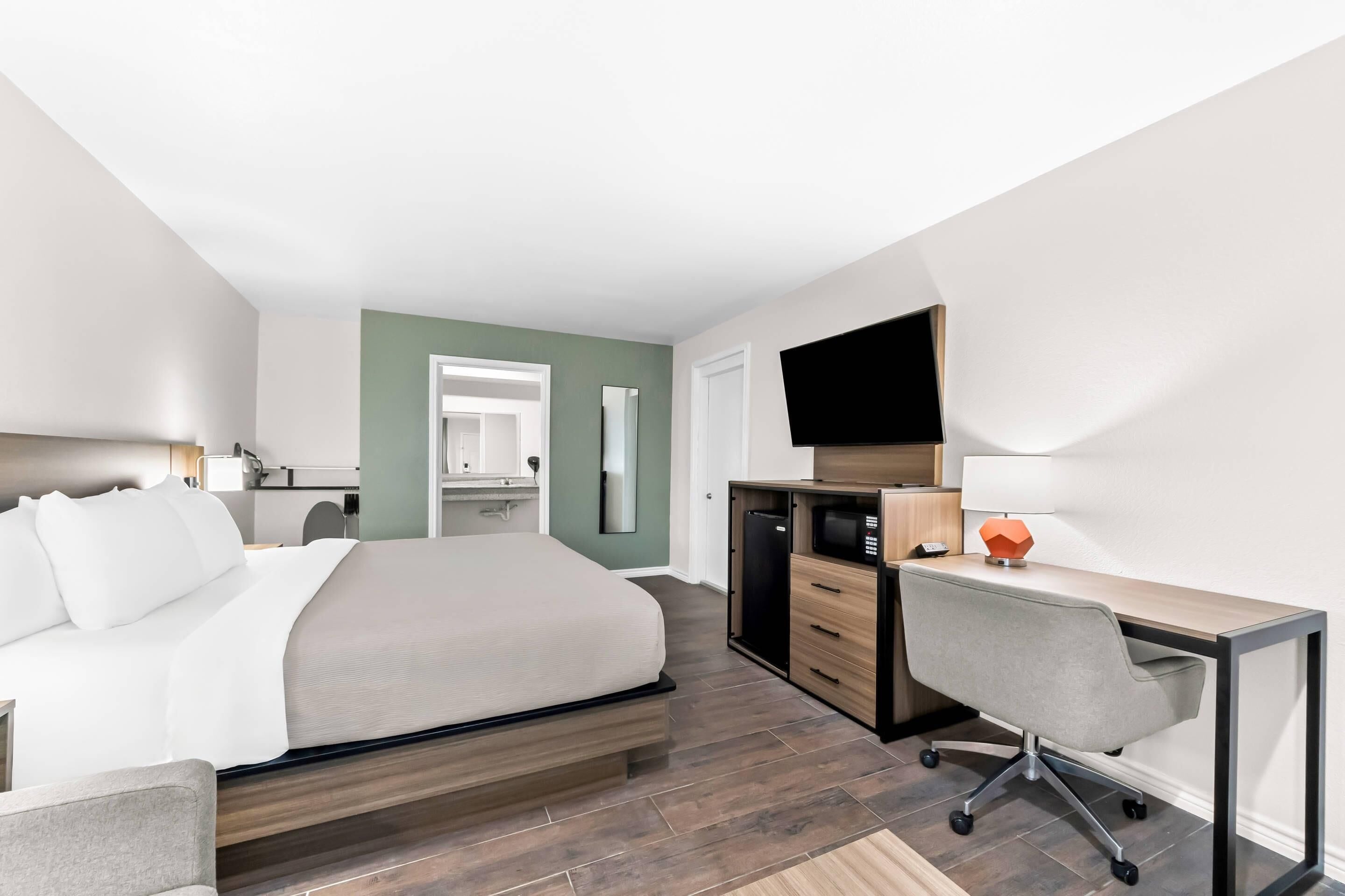 A modern hotel room with a bed, desk, chair, and a TV.